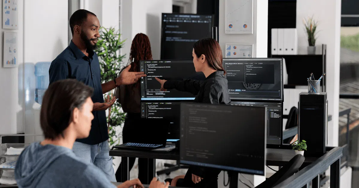 A group of developers discussing code in an open-plan office, symbolizing teamwork and flexibility in outsourced development environments.